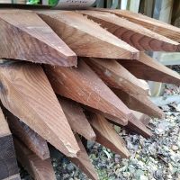 Pile of pointed fence posts laid vertically (approximately 14) with pointed end facing the camera
