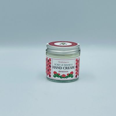 Screw top glass jar of honey and beeswax hand cream wrapped with a branded sticker, white background.