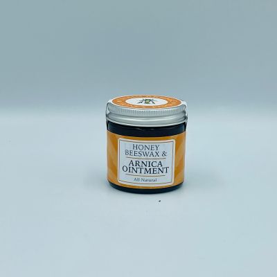 Screw top glass jar of honey and beeswax arnica ointment wrapped with a branded sticker, white background.