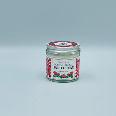 Screw top glass jar of honey and beeswax hand cream wrapped with a branded sticker, white background.